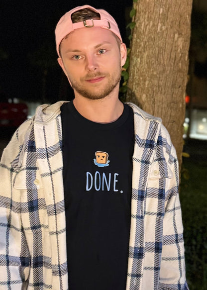 Man wearing a black t-shirt with 'DONE' text, plaid shirt, and pink cap standing outdoors at night.