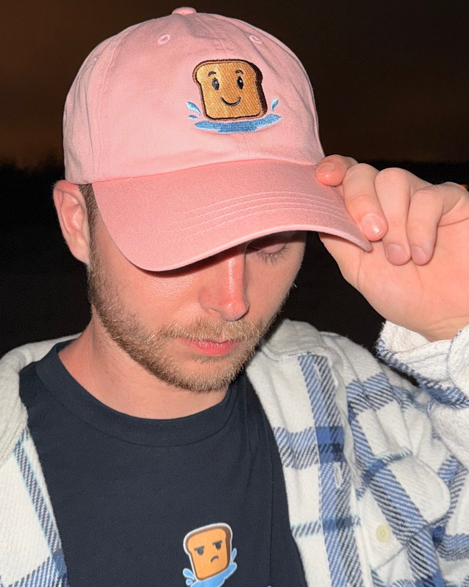 Person wearing a pink cap and black t-shirt with graphics and text against a dark background